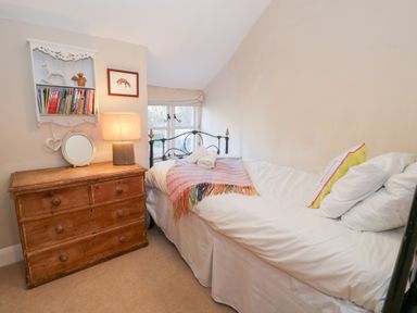 A bedroom with a single bed next to a wooden chest of drawers with a lamp and books on a wall shelf at Glandwr Cottage in Llanbedr
