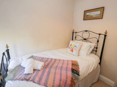 A bed with a pink and striped blanket and a floral pillow in a bedroom at Glandwr Cottage in Llanbedr