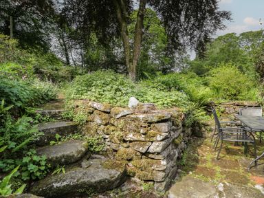 A garden with stone steps, a wall, and a table with chairs at Glandwr Cottage Llanbedr