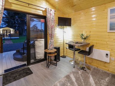 An interior room with wooden walls a small table with two chairs a wall mounted television and sliding glass door at Binevanagh Cabin Magilligan near Castlerock