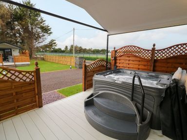 An outdoor deck with a hot tub and wooden fencing overlooking a yard and a small building at Binevanagh Cabin in Magilligan near Castlerock