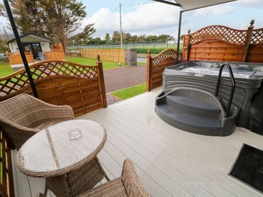 An outdoor patio with a hot tub and wicker chairs around a glass table at Binevanagh Cabin in Magilligan near Castlerock