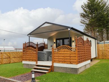 A cabin with a covered porch and wooden railing with steps on a grassy lawn at Binevanagh Cabin in Magilligan near Castlerock