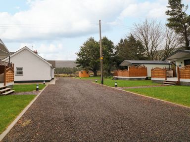A gravel driveway between white buildings with wooden fences and green lawns at Binevanagh Cabin in Magilligan near Castlerock