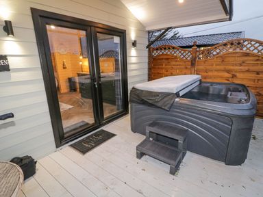 An outdoor deck area with a hot tub steps and glass double doors leading inside at MUSSENDEN CABIN Magilligan near Castlerock