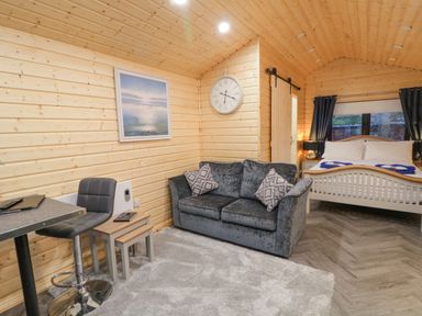 A wooden cabin interior with a sofa table and chair a bed with pillows and towels and a wall clock at MUSSENDEN CABIN Magilligan near Castlerock