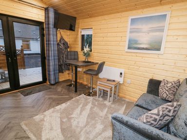 A living area with a sofa a small dining table two chairs a wall-mounted TV and a framed painting at MUSSENDEN CABIN Magilligan near Castlerock
