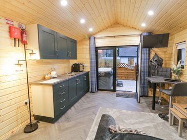 A small kitchen and living space with dark cabinets a sink and coffee machine next to a glass door leading outside and a small dining table with chairs at MUSSENDEN CABIN Magilligan near Castlerock