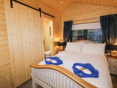 A bedroom with a double bed with white bedding blue towels bedside tables with lamps and a sliding wooden door at MUSSENDEN CABIN Magilligan near Castlerock