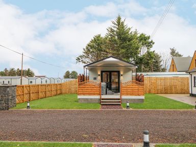 A small cabin with a porch and wooden fencing on a grass lawn at Benone Cabin in Magilligan near Castlerock