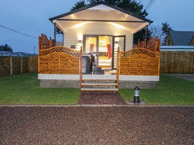 A small cabin with a wooden porch and steps leading up to a glass door at Benone Cabin in Magilligan near Castlerock