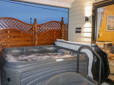 An outdoor hot tub with wooden lattice fencing and an open door to a room at Benone Cabin Magilligan near Castlerock