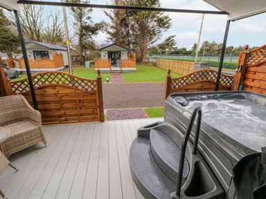 An outdoor deck with a hot tub wicker chair and wooden fence with cabins and grass in the background at Benone Cabin in Magilligan near Castlerock