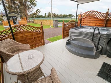 An outdoor patio with a hot tub two wicker chairs and a glass top table at Benone Cabin in Magilligan near Castlerock