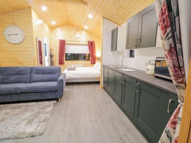An open room with a blue sofa rug kitchen cabinets and a bed inside Benone Cabin in Magilligan near Castlerock