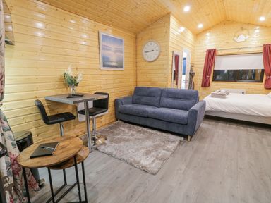 A living area with a blue sofa a dining table with two chairs a bed and wooden walls at Benone Cabin in Magilligan near Castlerock