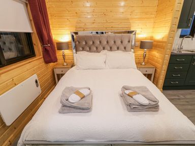 A bedroom with a double bed with white bedding two bedside tables with lamps and wooden walls at Benone Cabin in Magilligan near Castlerock