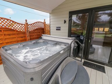 An outdoor hot tub with steps on a covered patio next to glass doors and wooden fence at Benone Cabin in Magilligan near Castlerock