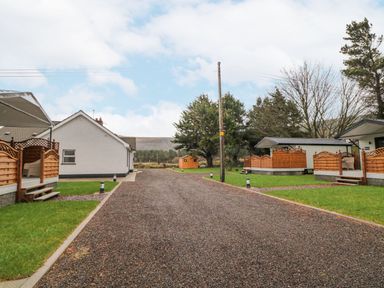 A driveway between white houses with wooden fences and green lawns at Benone Cabin in Magilligan near Castlerock