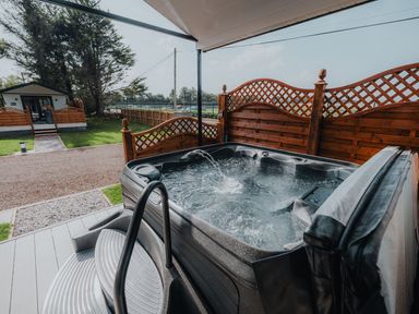 An outdoor hot tub with water jets near a wooden privacy fence and a small house in the background at Benone Cabin Magilligan near Castlerock