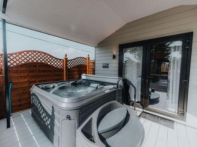 An outdoor covered deck with a hot tub, steps, wooden privacy fencing, and glass doors at Benone Cabin in Magilligan near Castlerock