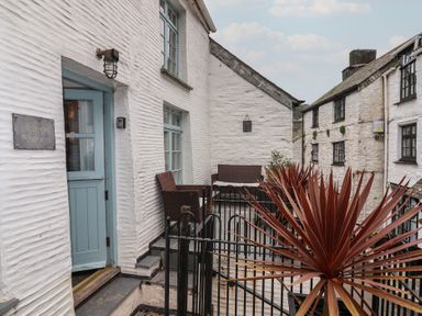An outdoor patio area with chairs and a table beside white stone buildings at Teana Cottage in Polperro