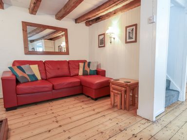 A living room with a red sectional sofa and nesting tables on a wooden floor at Teana Cottage in Polperro