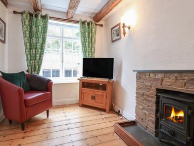 A living room with a red armchair green curtains a wooden TV stand with a TV and a fireplace at Teana Cottage in Polperro