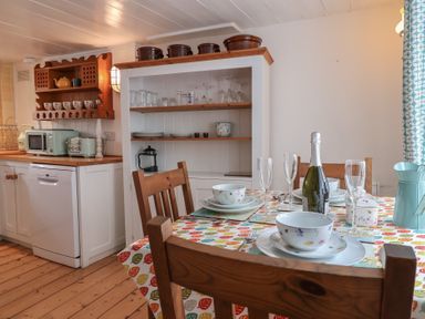 A kitchen dining area with a wooden table set with plates bowls glasses and a bottle in Teana Cottage Polperro