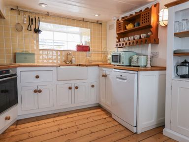 A kitchen with white cabinets wooden countertops and utensils hanging by a window at Teana Cottage in Polperro