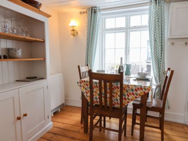 A dining area with wooden chairs and table with colorful tablecloth near window with patterned curtains at Teana Cottage Polperro