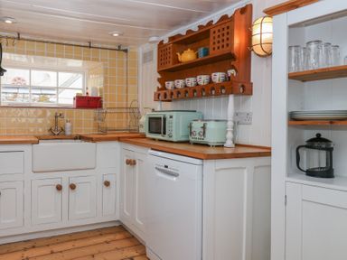 A kitchen with wooden countertops white cabinets a farmhouse sink toaster microwave and dish rack at Teana Cottage in Polperro