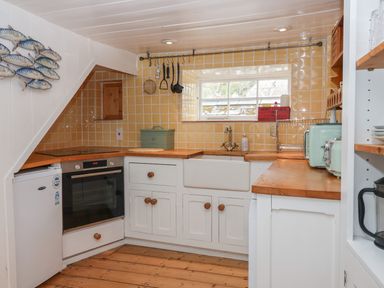 A kitchen with white cabinets wooden countertops yellow tile backsplash and various kitchen appliances at Teana Cottage in Polperro