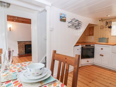 A kitchen with white cabinets and wooden floor with a dining table set with dishes and glasses at Teana Cottage in Polperro