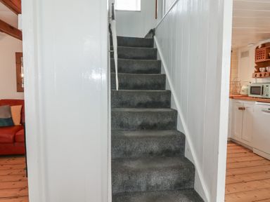 A carpeted staircase surrounded by white walls with a kitchen on the right and a living area with a red sofa on the left at Teana Cottage in Polperro
