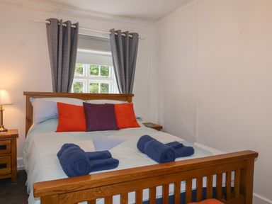 A bedroom with a wooden bed frame a bed with orange and purple cushions blue towels on the bed and nightstands with lamps at Teana Cottage in Polperro
