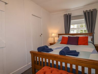 A bedroom with a wooden bed with folded towels on it two bedside tables with a lamp and window with curtains at Teana Cottage in Polperro