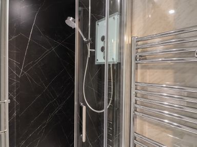 A shower enclosure with a handheld showerhead and a chrome towel radiator in a bathroom at Teana Cottage in Polperro