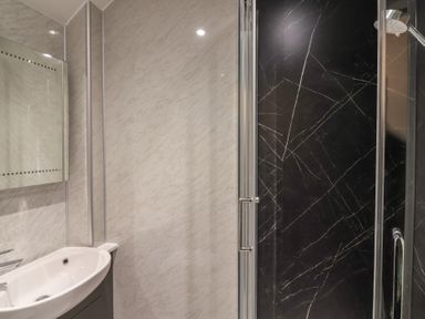 A bathroom with a white sink and a glass door shower with black marble walls at Teana Cottage Polperro