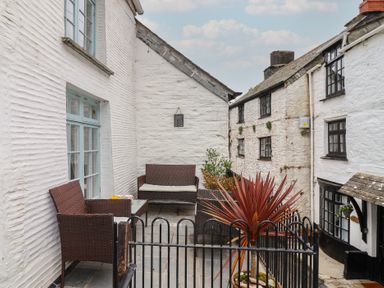 An outdoor patio area with wicker seating and a potted plant surrounded by white buildings at Teana Cottage Polperro