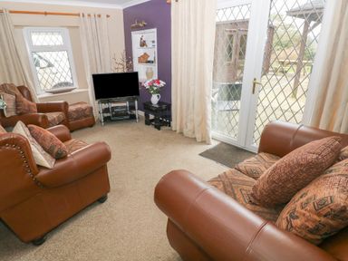 A living room with brown leather sofas a television on a stand and glass doors leading outside at Greenhaven in Narberth