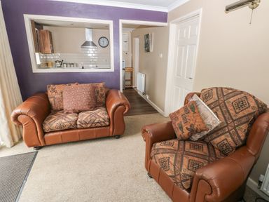 A living room with two patterned armchairs and a window opening to a kitchen at Greenhaven in Narberth