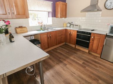 A kitchen with wooden cabinets a white countertop a window above the sink a stove a stainless steel hood a refrigerator and a wooden floor at Greenhaven in Narberth