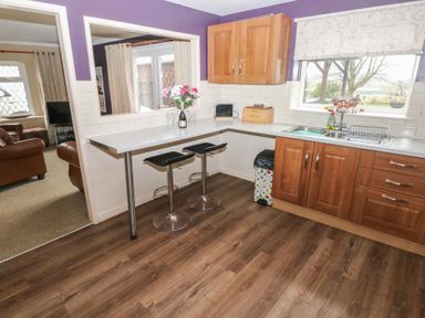 A kitchen with wooden cabinets two black bar stools a sink and a countertop with a flower vase at Greenhaven in Narberth