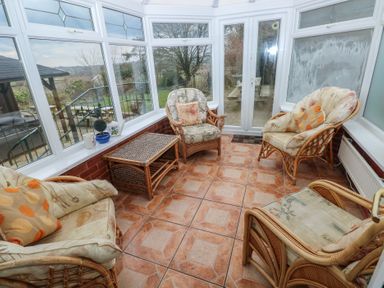 A conservatory with wicker chairs and a wicker table with cushions and potted plants at Greenhaven in Narberth