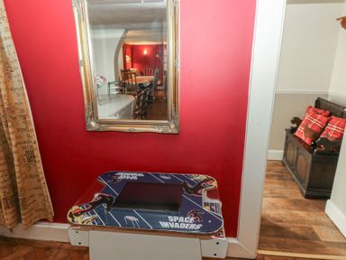 A corner with a space invaders arcade game against a red wall with a mirror reflecting a dining room at Greenhaven in Narberth