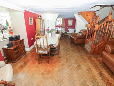 A dining room with wooden chairs a table with a tablecloth flowers in a vase wooden cabinets a staircase and leather armchairs at Greenhaven in Narberth