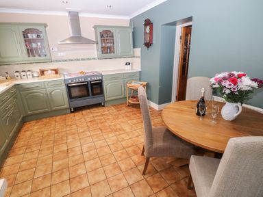 A kitchen with green cabinets a stove a round wooden table with chairs flowers and a bottle at Greenhaven in Narberth