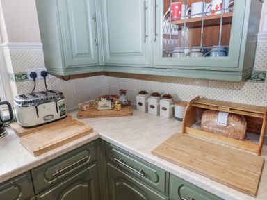 A kitchen corner with green cabinets a toaster jars a bread box and a tray with bread and butter at Greenhaven Narberth