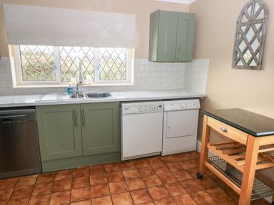 A kitchen with green cabinets a double sink a dishwasher a washing machine a wooden trolley and a wall mirror at Greenhaven in Narberth